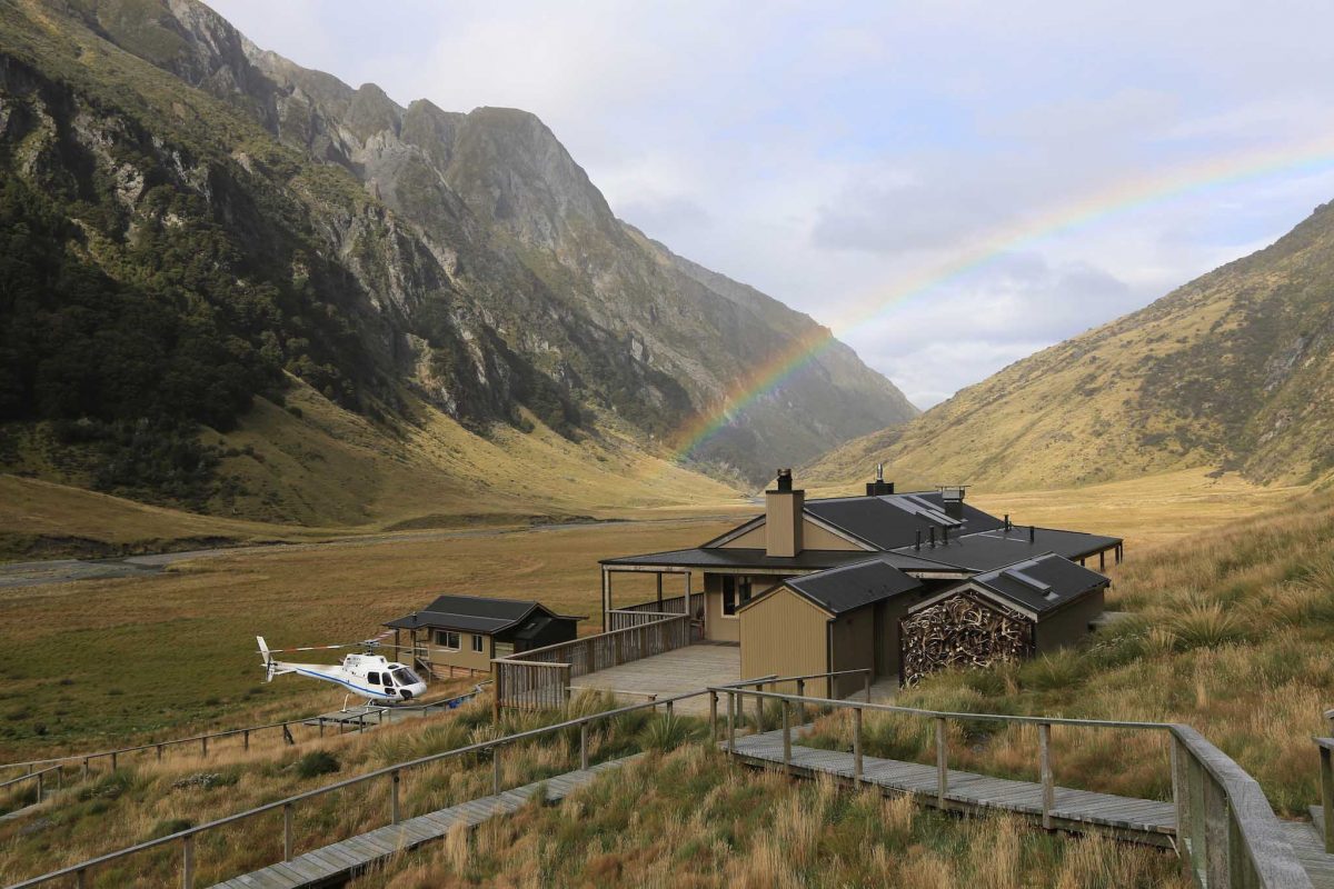 A helicopter awaits outside of Huka Lodge, surrounded by mountains and a rainbow