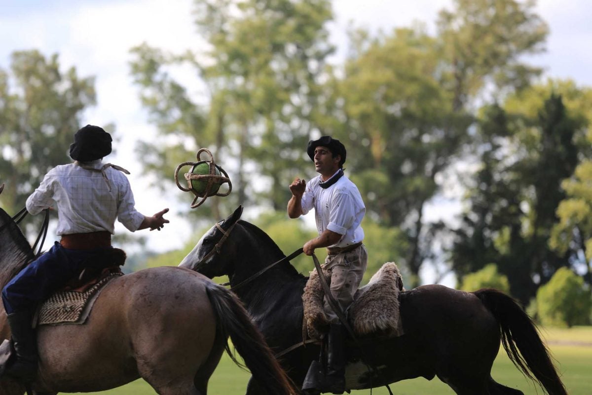Two gauchos on horseback pass a ball